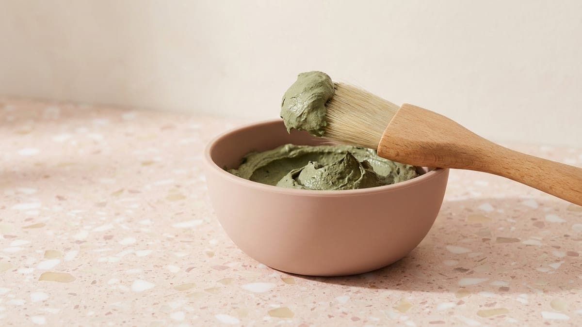 Bol en silicone rose rempli d'argile verte, pinceau large en bois posé dessus