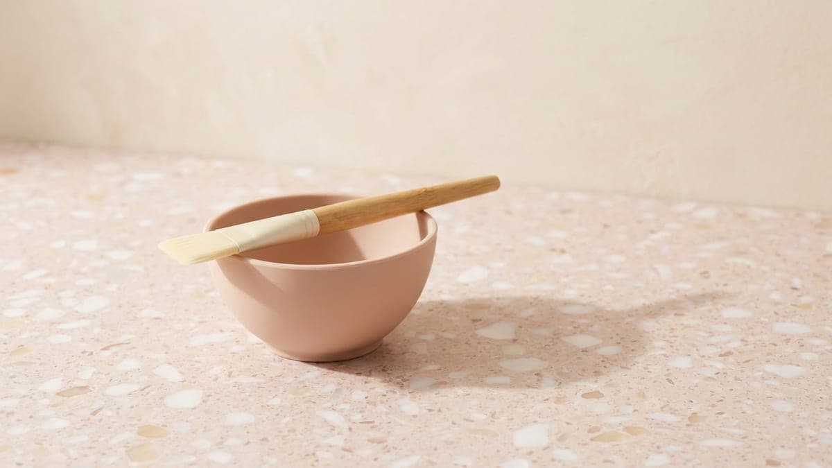 Bol en silicone rose poudré, un pinceau à masque à manche en bois posé en travers