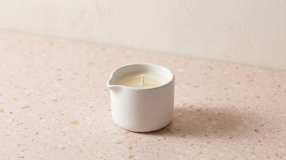 Bougie de massage dans un pot en céramique blanche à bec verseur, cire crème et mèche éteinte