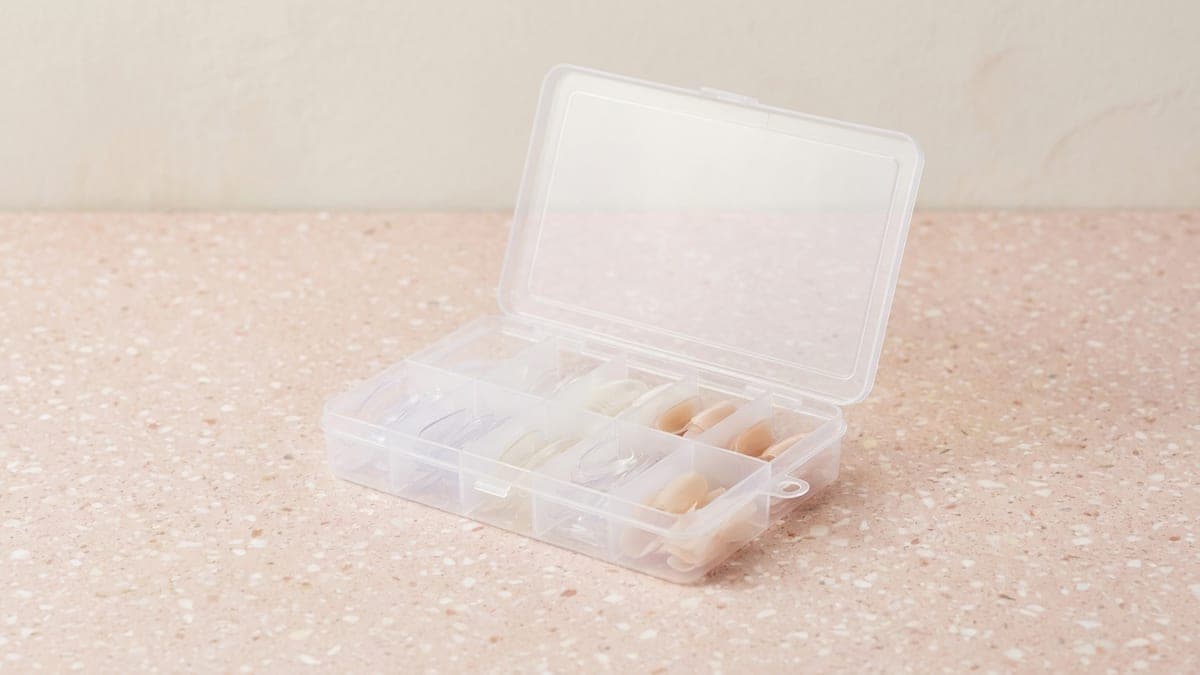Boîte à compartiments remplie de capsules d'ongles transparentes et naturelles