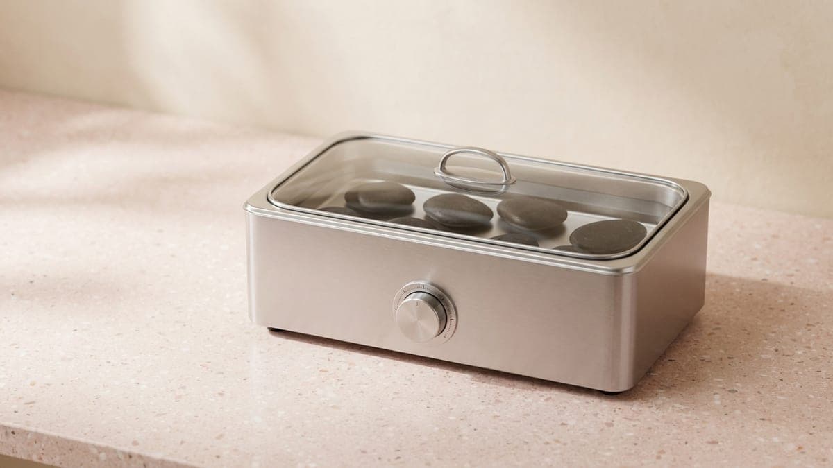 Chauffe-pierres rectangulaire en inox à bouton de réglage, dont le couvercle en verre laisse voir des pierres noires dans l'eau