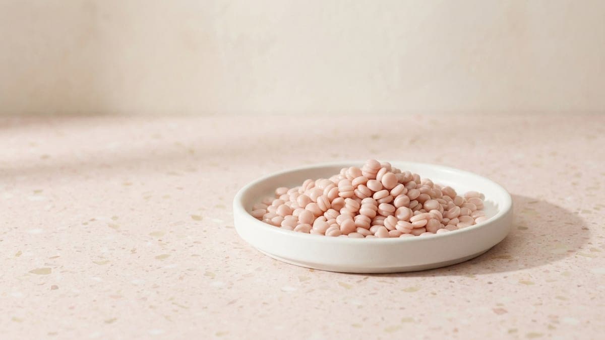 Petit tas de perles de cire rose pâle dans une coupelle en céramique blanche