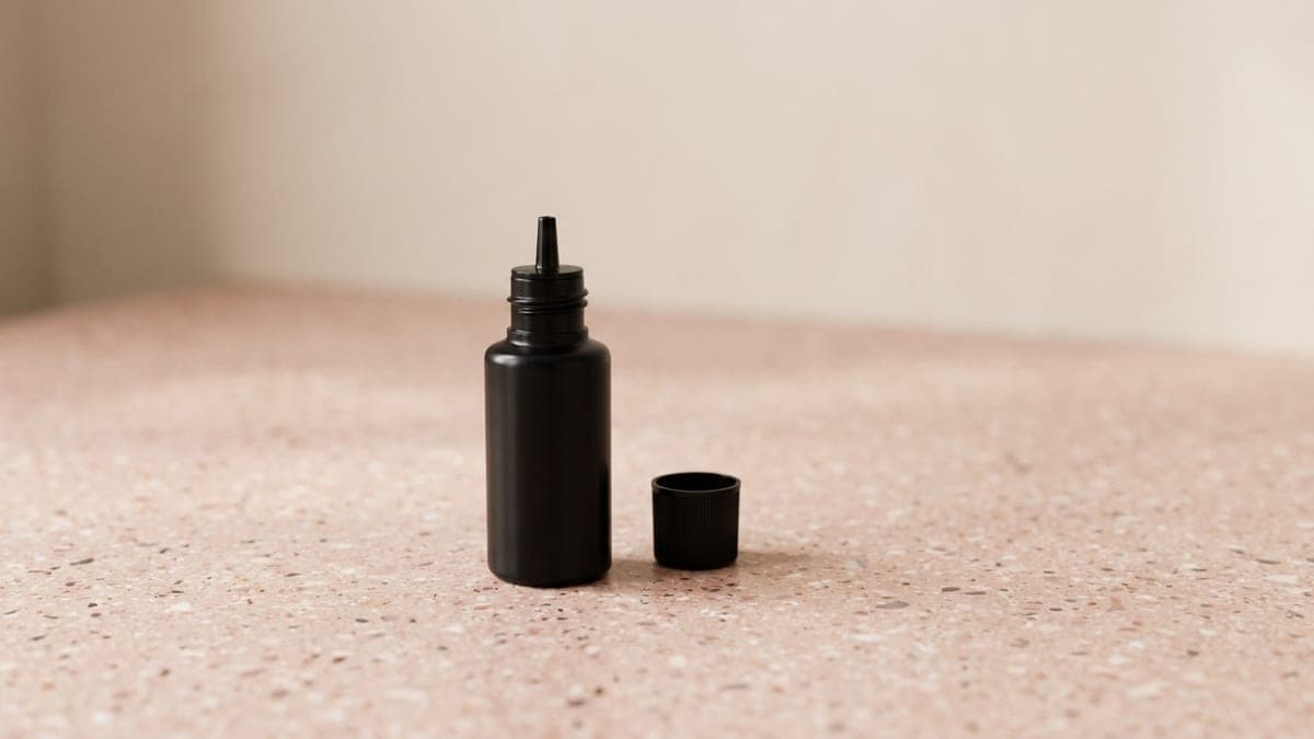 Petit flacon noir de colle pour extension de cils à embout fin, son bouchon posé à côté
