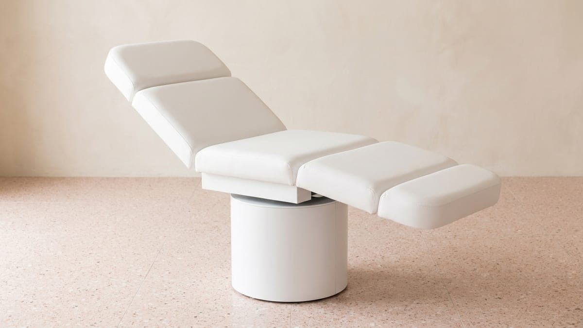 Fauteuil de soin électrique en simili-cuir blanc, dossier relevé et repose-jambes articulé, sur colonne blanche