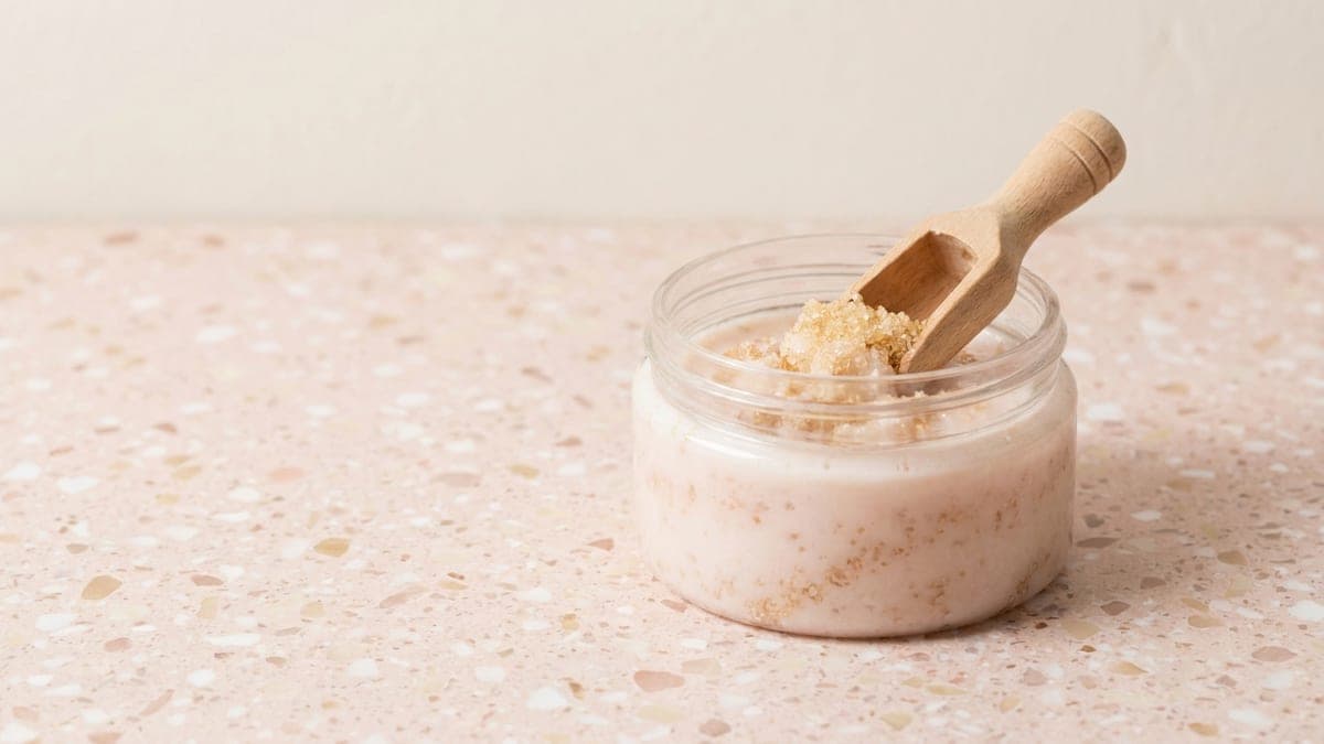 Pot ouvert de gommage corps aux grains de sucre, cuillère doseuse en bois plantée dedans