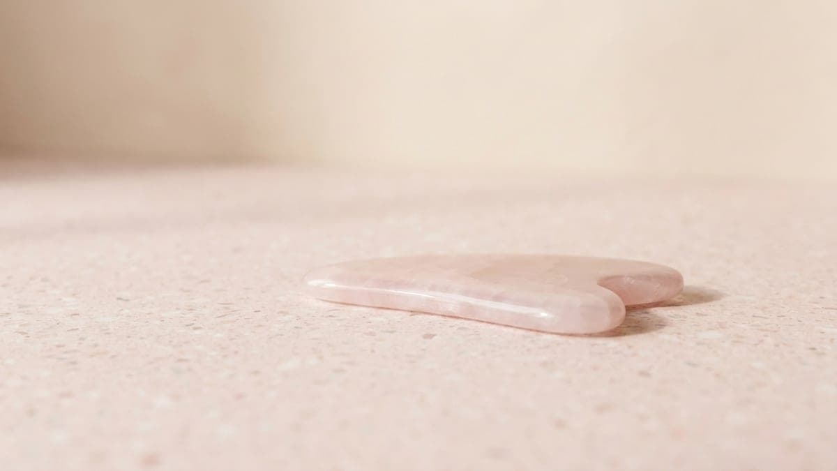 Pierre de gua sha en quartz rose poli, posée à plat, bord incurvé à encoche