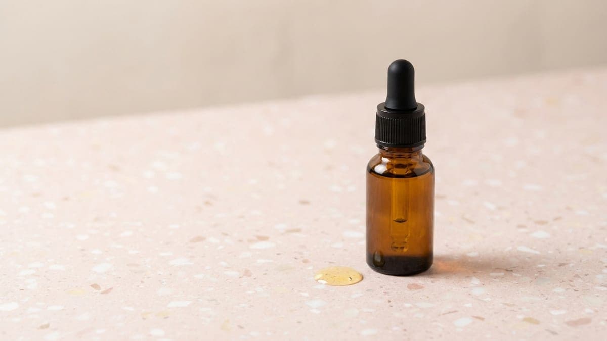 Flacon compte-gouttes ambré d'huile pour cuticules, une goutte d'huile à côté