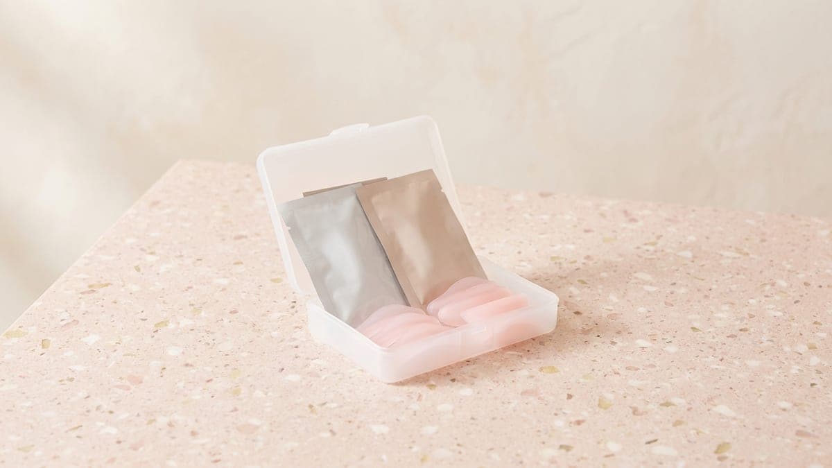 Petit étui blanc ouvert contenant deux sachets et des bigoudis en silicone rose de plusieurs tailles