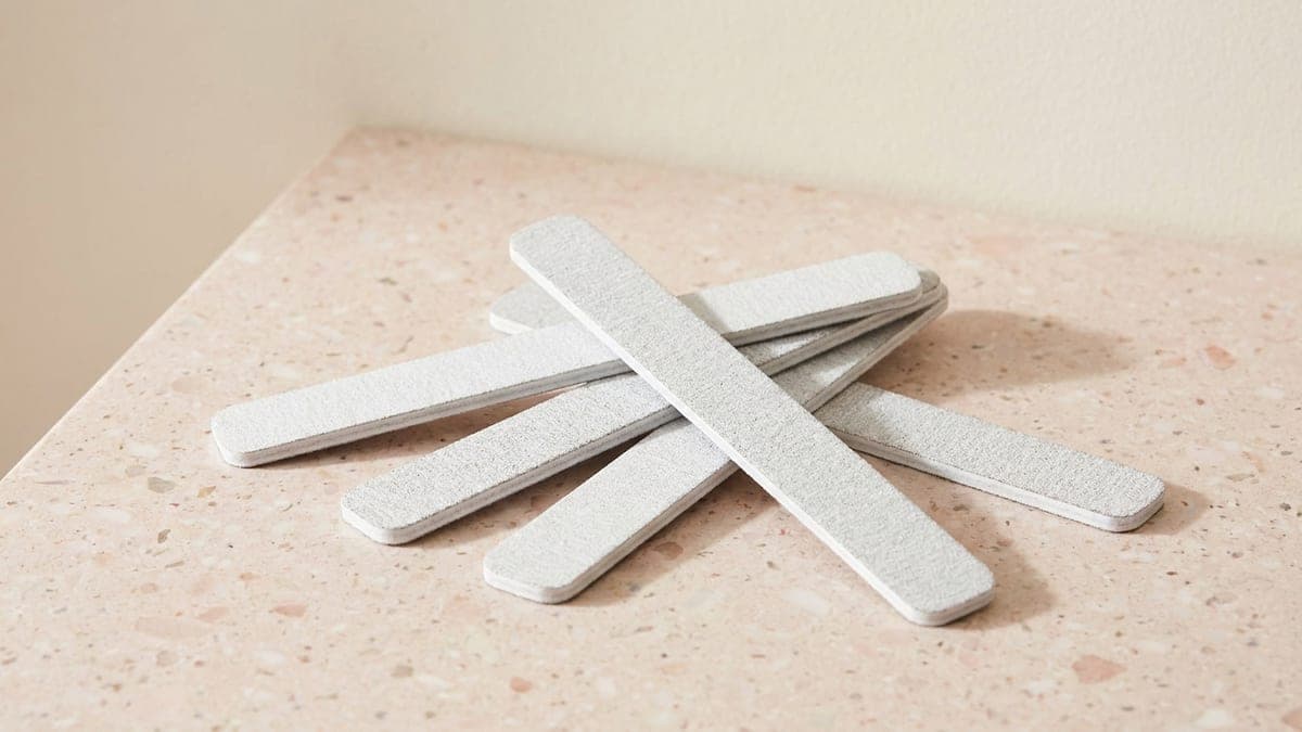 Quelques limes à ongles jetables blanches posées en vrac sur un plan de travail rose poudré