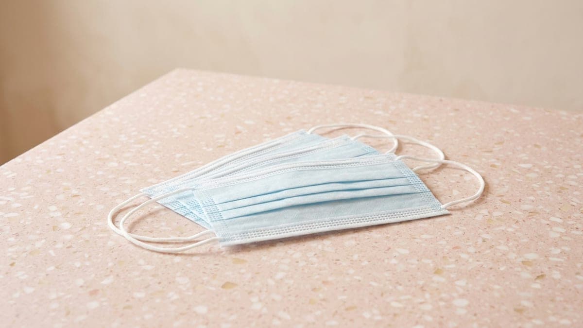 Trois masques jetables bleu clair plissés, à élastiques blancs, posés à plat