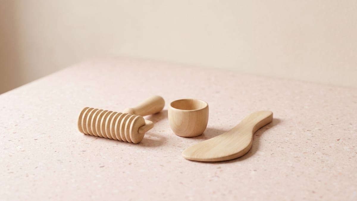 Trois outils de massage en bois clair : un rouleau cannelé à manche, une coupelle et une palette incurvée