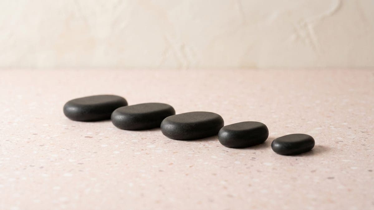 Cinq galets de basalte noirs, lisses et plats, alignés du plus grand au plus petit
