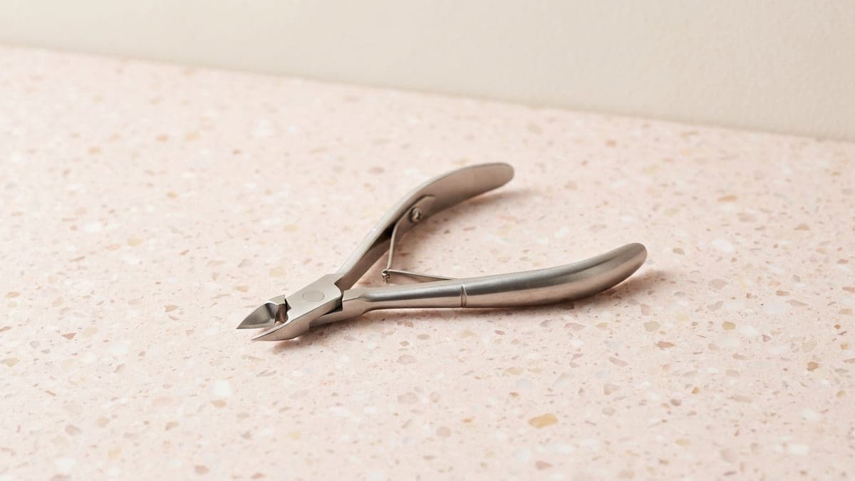 Pince à envies en inox, légèrement ouverte, posée sur un plan de travail rose poudré