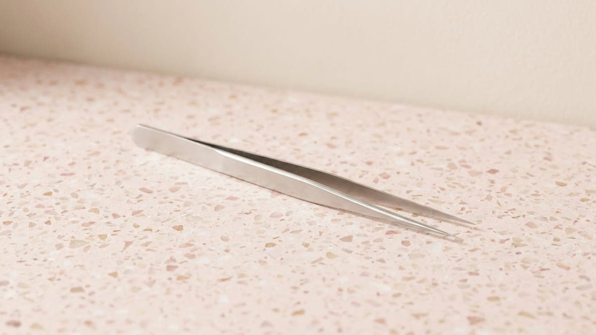 Pince d'isolation en acier inoxydable aux longues pointes droites très fines, posée en diagonale sur un plan en terrazzo rose