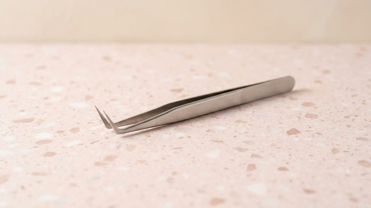Pince volume en acier inoxydable aux pointes coudées en L, posée sur un plan en terrazzo rose