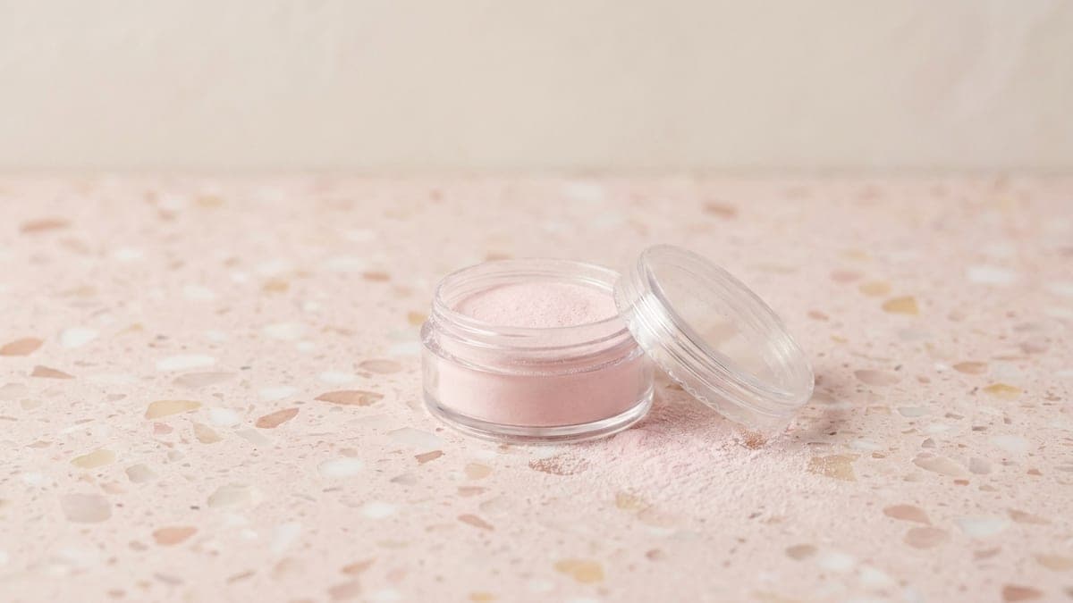 Pot de poudre acrylique rose pâle ouvert, un peu de poudre renversée