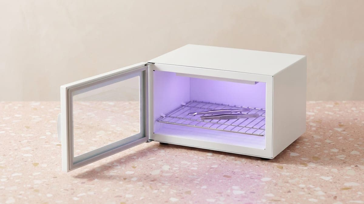 Boîte UV blanche ouverte, pinces posées sur une grille éclairée de violet