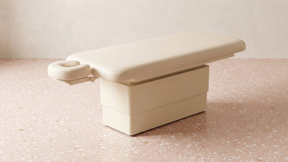 Table de massage fixe à plateau crème capitonné, têtière ronde à une extrémité, montée sur un socle plein