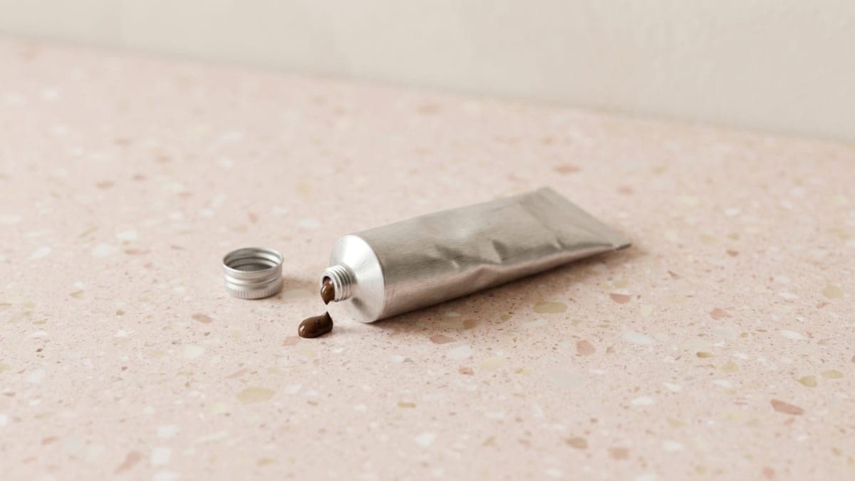 Petit tube métallique de crème de teinture brun foncé, bouchon ôté posé à côté