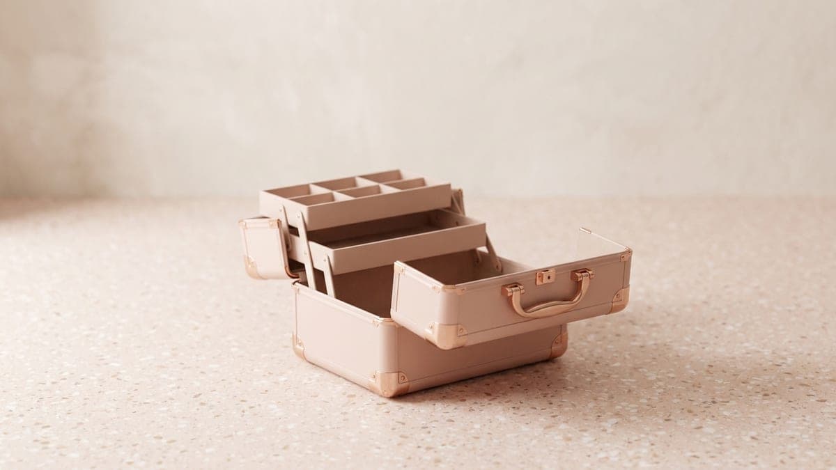 Vanity rigide rose poudré à coins cuivrés, ouvert sur ses plateaux à compartiments