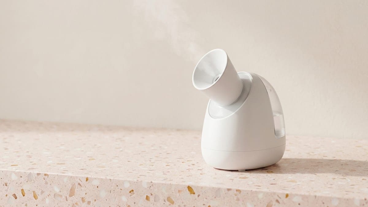 Sauna facial de table blanc, réservoir transparent et cône tourné vers l'avant, un filet de vapeur
