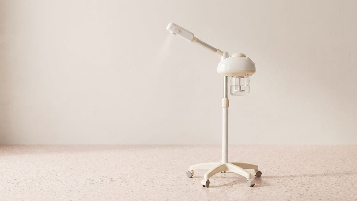 Vapozone blanc sur pied à cinq roulettes, réservoir transparent et bras orientable terminé par une buse