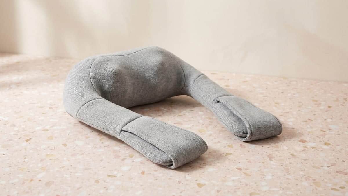 Masseur shiatsu en tissu gris chiné en forme de U, avec une anse à chaque extrémité, posé à plat sur un sol en terrazzo rose pâle