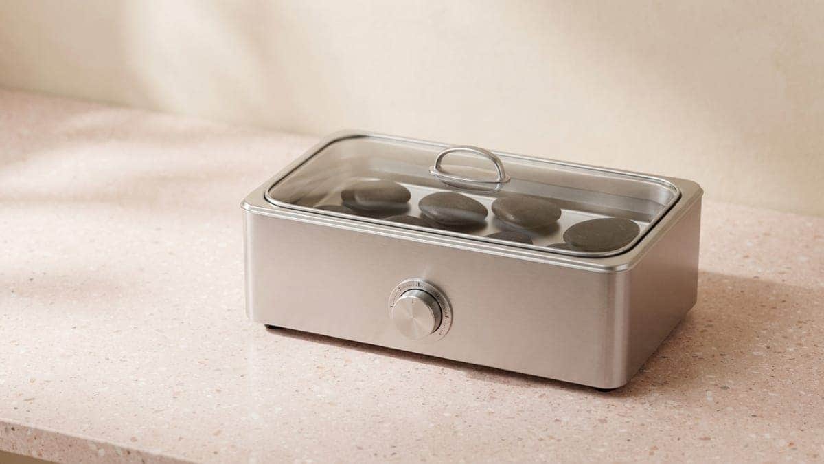 Chauffe-pierres rectangulaire en inox à bouton de réglage, dont le couvercle en verre laisse voir des pierres noires dans l'eau